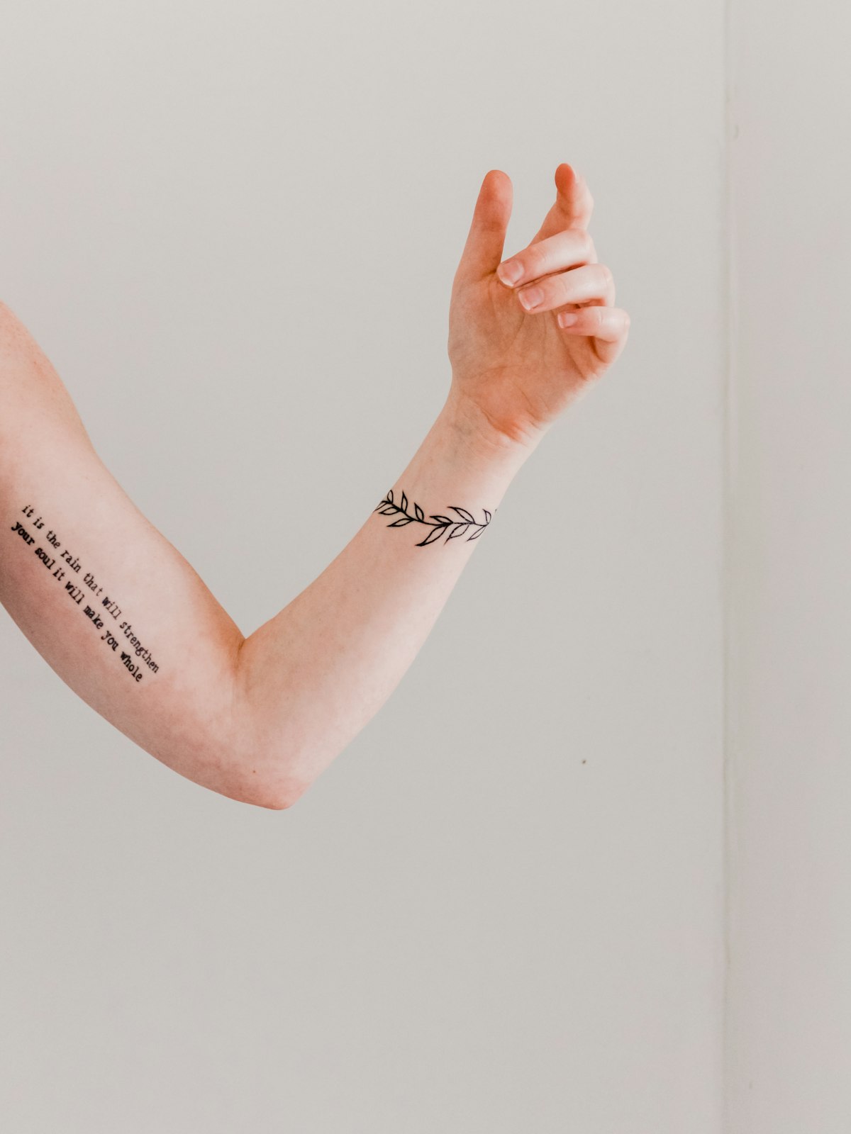Feines Fine-Line-Tattoo mit Schriftzug und Blätterranke am Unterarm