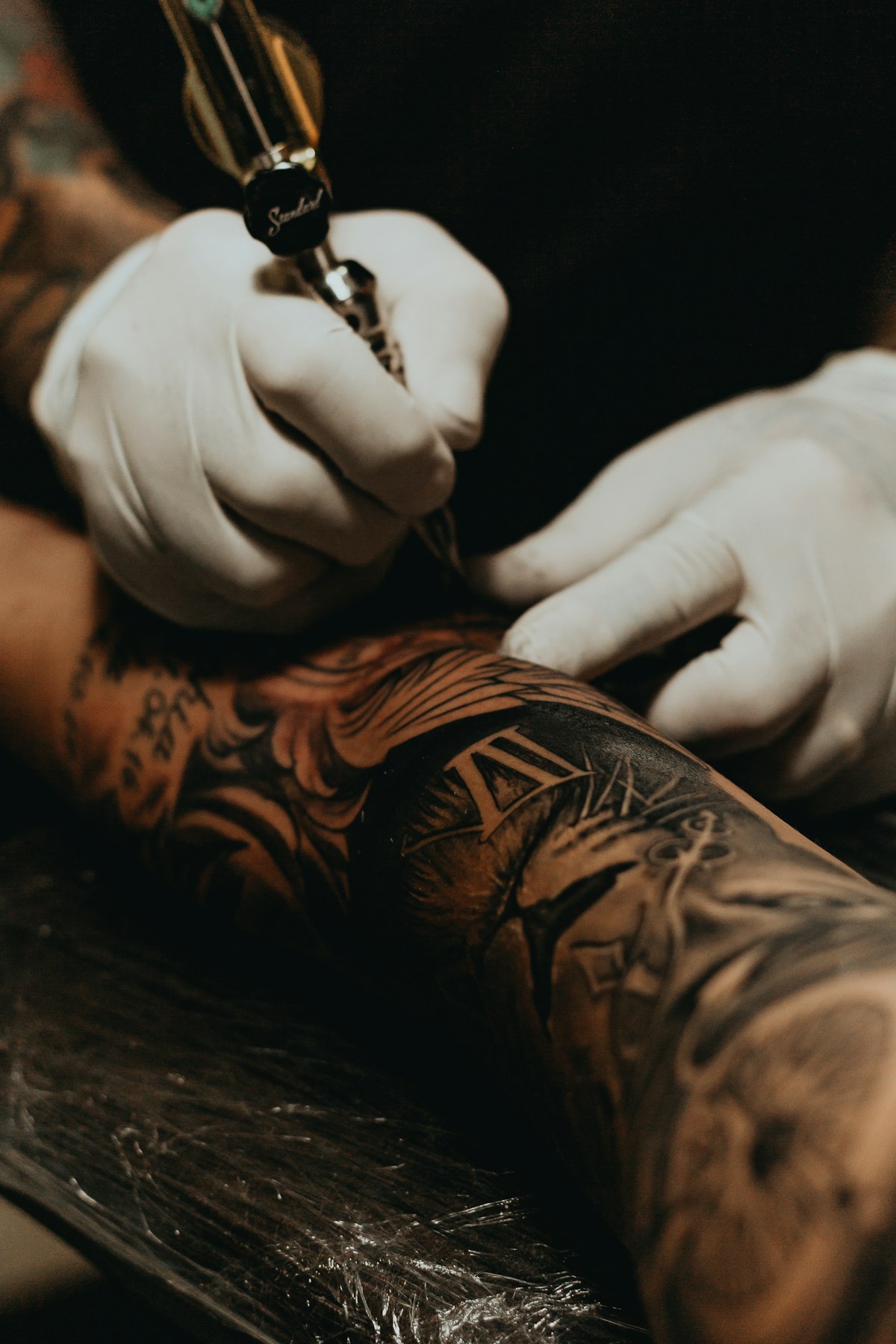 Tätowierer arbeitet konzentriert mit der Tattoomaschine am Unterarm eines Kunden